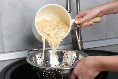 Photo of Woman draining boiled tagliatelle pasta into colander at sink in kitchen, closeup