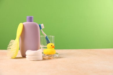 Photo of Baby accessories and bathing products on beige textured table against green background, space for text