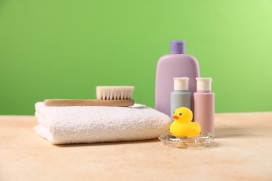 Photo of Baby accessories and bathing products on beige textured table against green background
