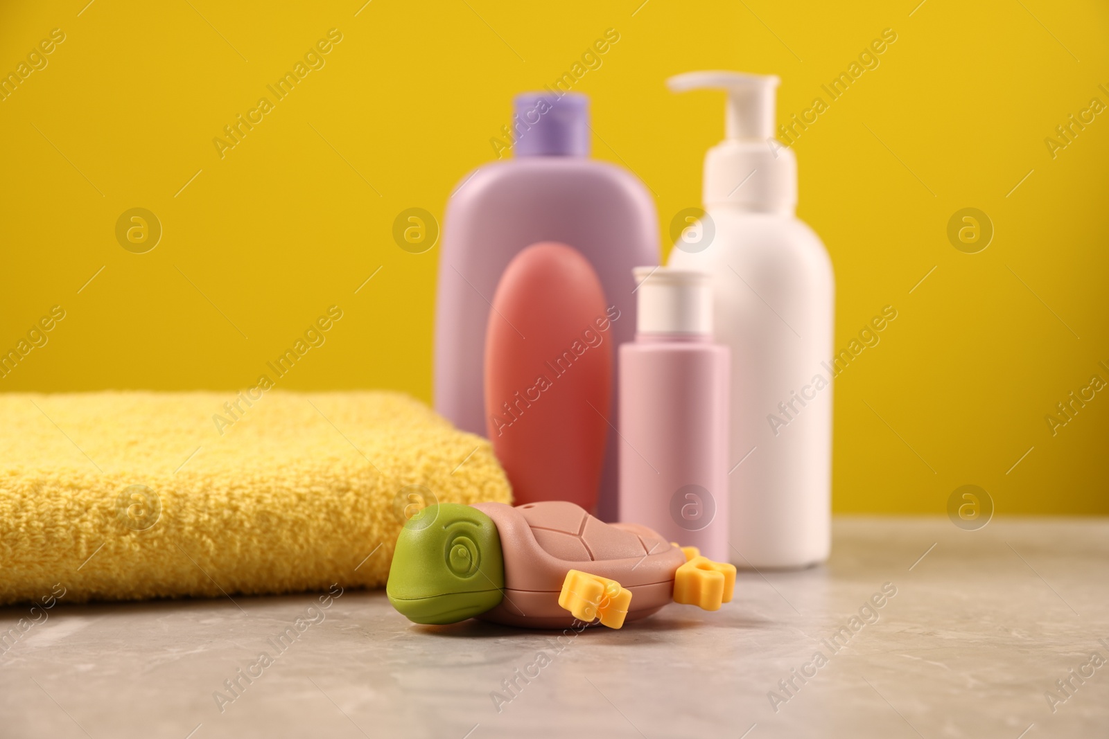 Photo of Baby accessories and bathing products on grey table against yellow background, closeup