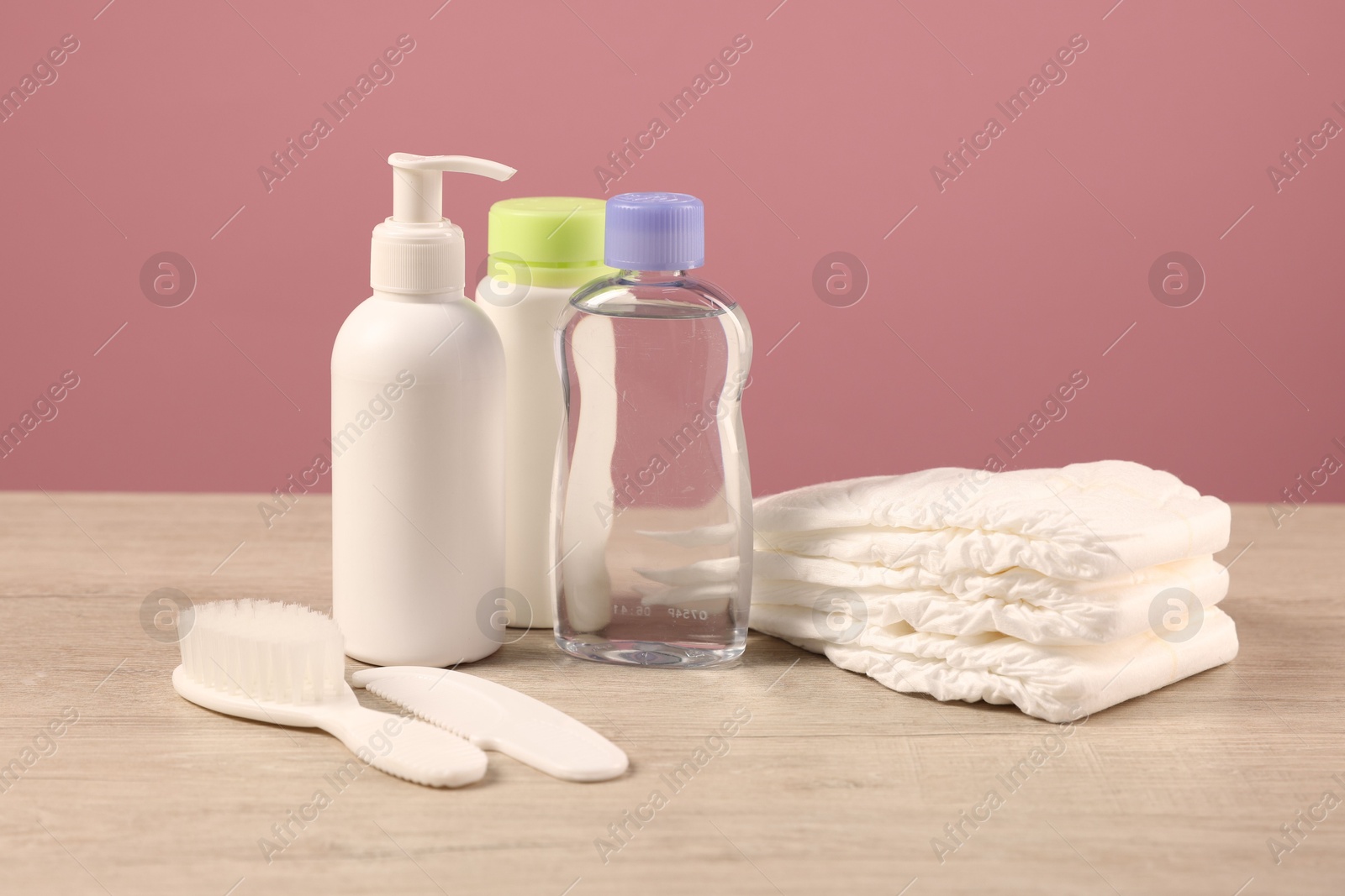 Photo of Baby accessories and bathing products on wooden table against pink background