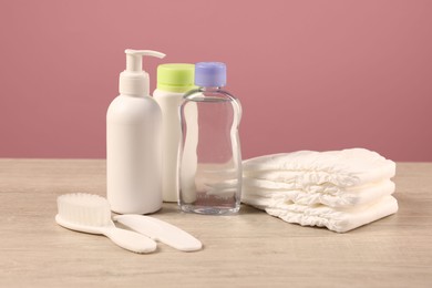 Photo of Baby accessories and bathing products on wooden table against pink background