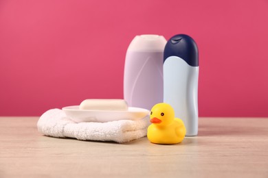 Photo of Baby accessories and bathing products on wooden table against pink background