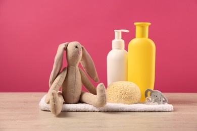 Photo of Baby accessories and bathing products on wooden table against pink background