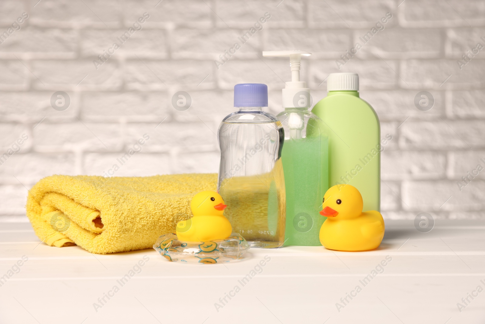 Photo of Baby accessories and bathing products on white wooden table near brick wall