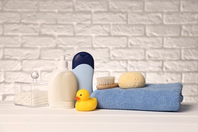 Photo of Baby accessories and bathing products on white wooden table near brick wall