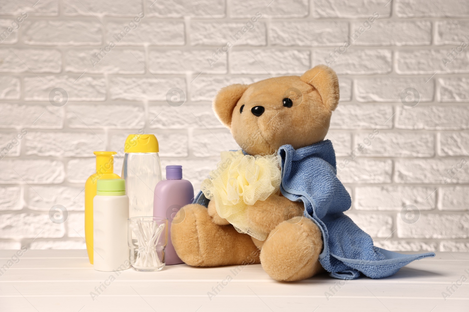 Photo of Baby accessories and bathing products on white wooden table near brick wall