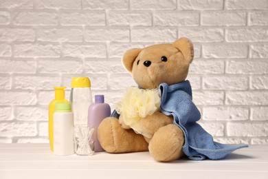 Photo of Baby accessories and bathing products on white wooden table near brick wall