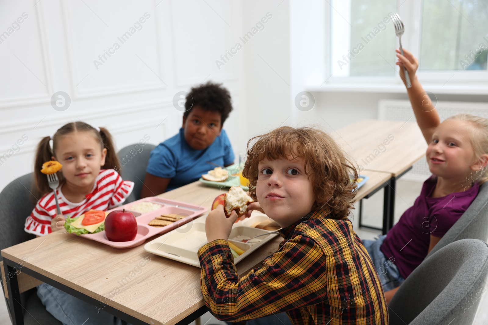 Little kids eating lunch at wooden table in school canteen Photo of Little kids eating lunch at wooden table in school canteen