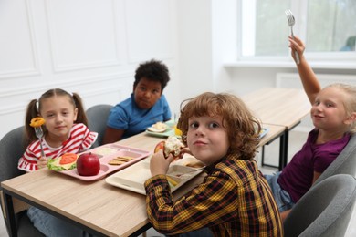 Photo of Little kids eating lunch at wooden table in school canteen