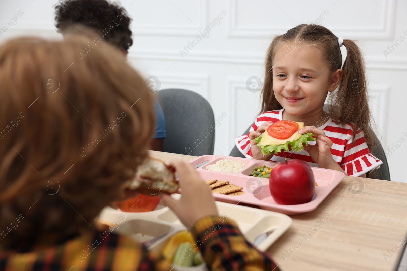 Little kids eating lunch at wooden table in school canteen Photo of Little kids eating lunch at wooden table in school canteen