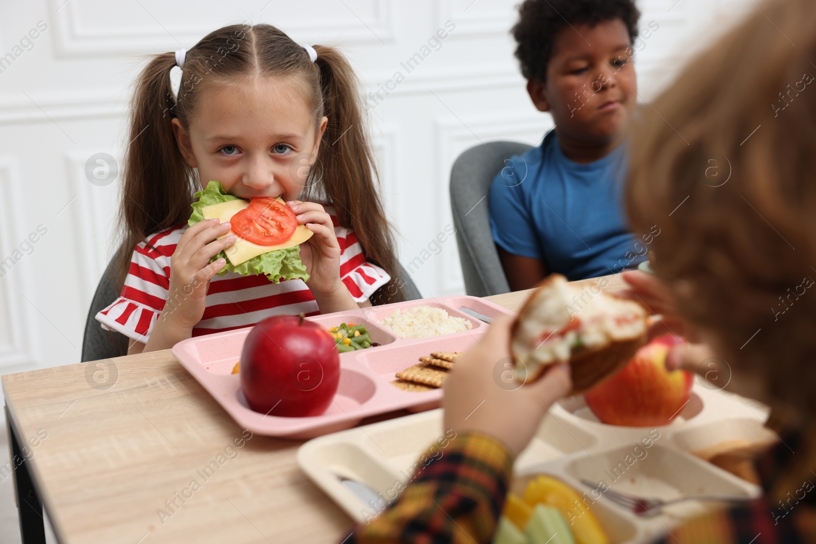 Little kids eating lunch at wooden table in school canteen Photo of Little kids eating lunch at wooden table in school canteen
