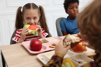 Photo of Little kids eating lunch at wooden table in school canteen