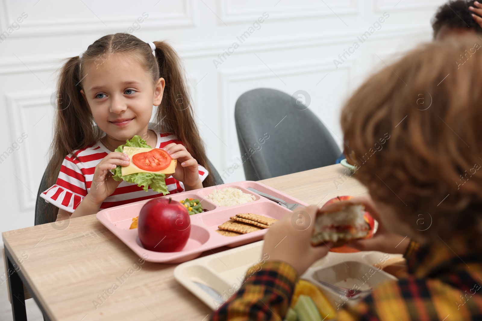Little kids eating lunch at wooden table in school canteen Photo of Little kids eating lunch at wooden table in school canteen