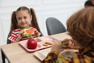Photo of Little kids eating lunch at wooden table in school canteen