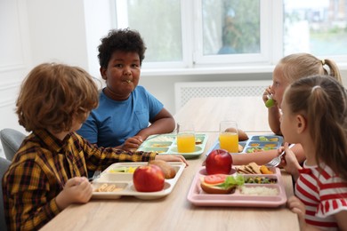 Photo of Little kids eating lunch at wooden table in school canteen
