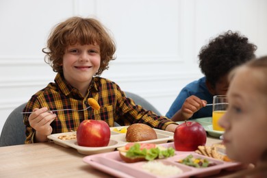 Photo of Little kids eating lunch at wooden table in school canteen