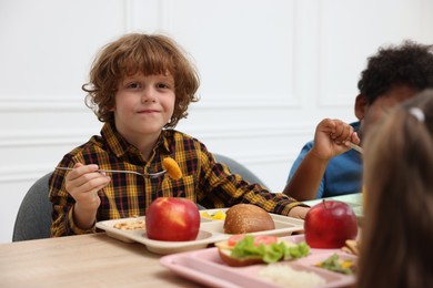 Photo of Little kids eating lunch at wooden table in school canteen
