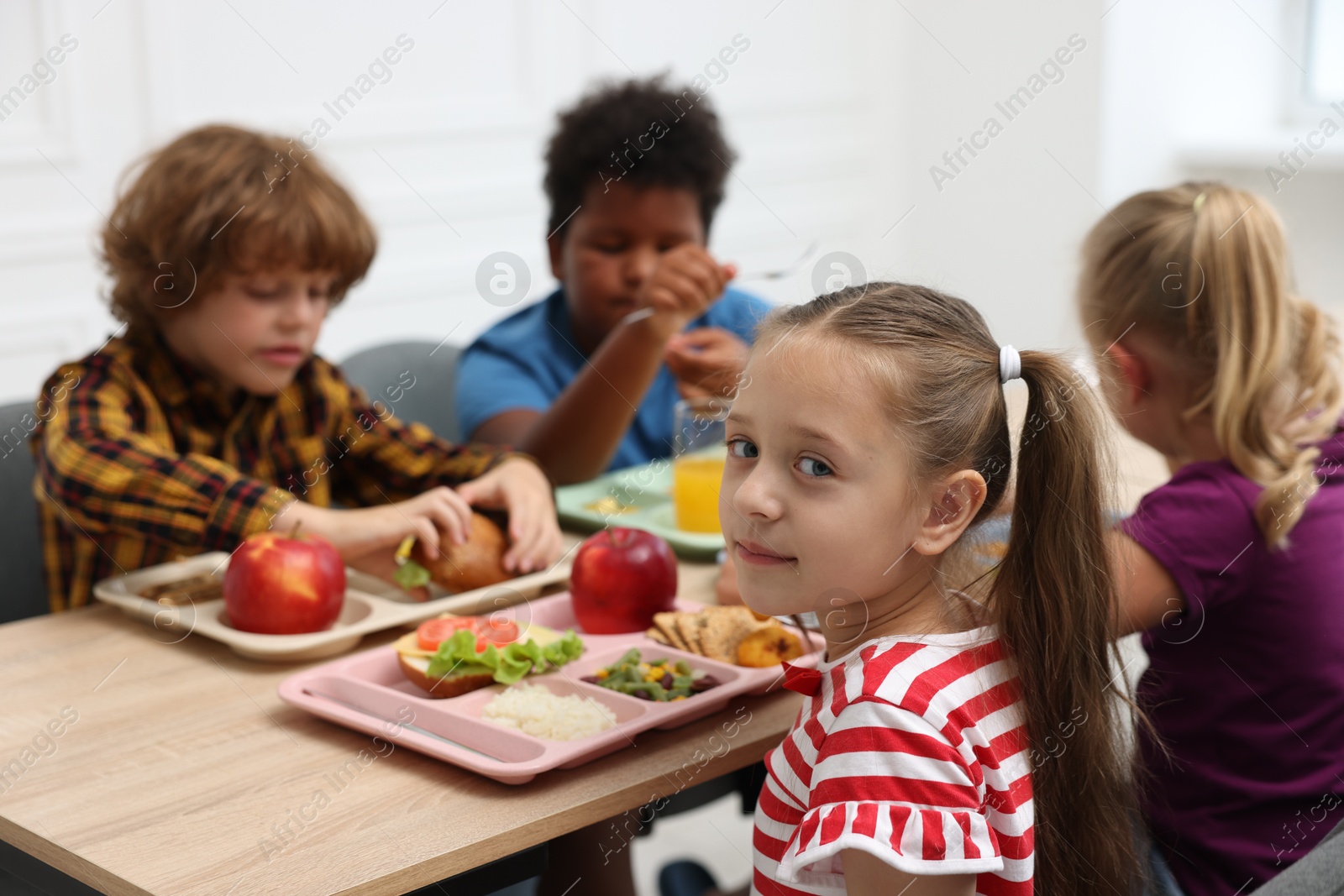 Little kids eating lunch at wooden table in school canteen Photo of Little kids eating lunch at wooden table in school canteen