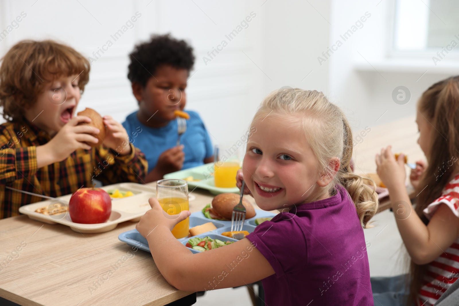 Little kids eating lunch at wooden table in school canteen Photo of Little kids eating lunch at wooden table in school canteen