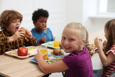 Photo of Little kids eating lunch at wooden table in school canteen