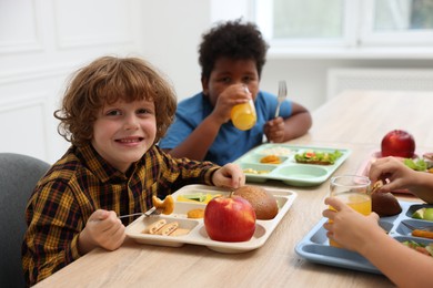 Photo of Little kids eating lunch at wooden table in school canteen