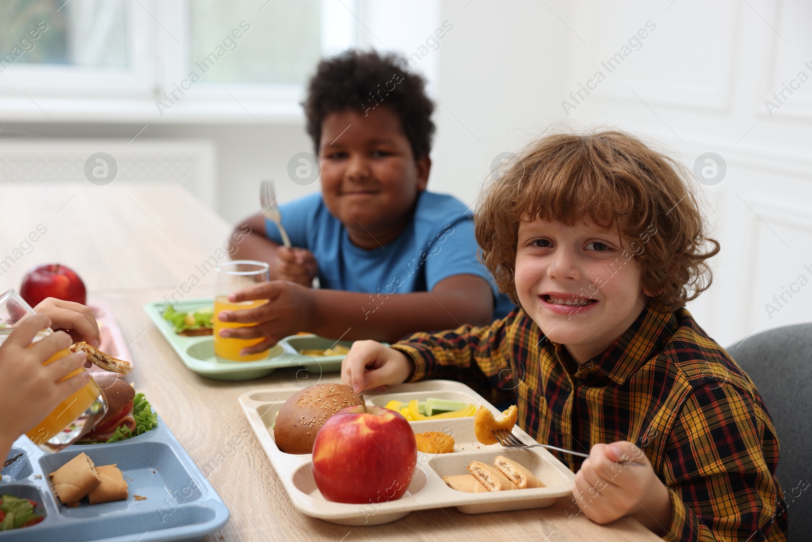 Little kids eating lunch at wooden table in school canteen Photo of Little kids eating lunch at wooden table in school canteen
