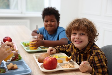 Photo of Little kids eating lunch at wooden table in school canteen