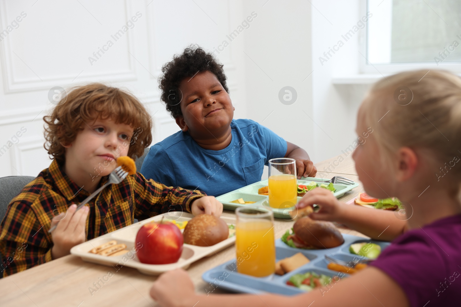 Little kids eating lunch at wooden table in school canteen Photo of Little kids eating lunch at wooden table in school canteen