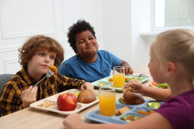 Photo of Little kids eating lunch at wooden table in school canteen