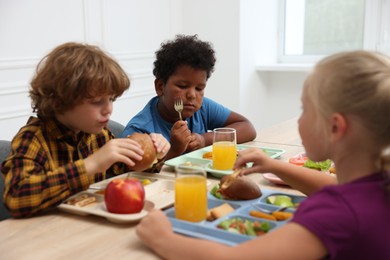 Photo of Little kids eating lunch at wooden table in school canteen