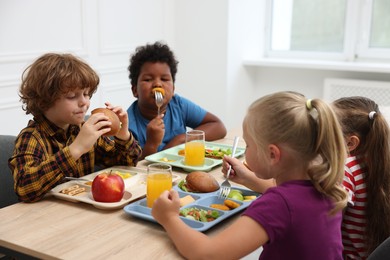 Photo of Little kids eating lunch at wooden table in school canteen