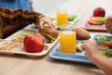 Photo of Little kids eating lunch at wooden table in school canteen, closeup