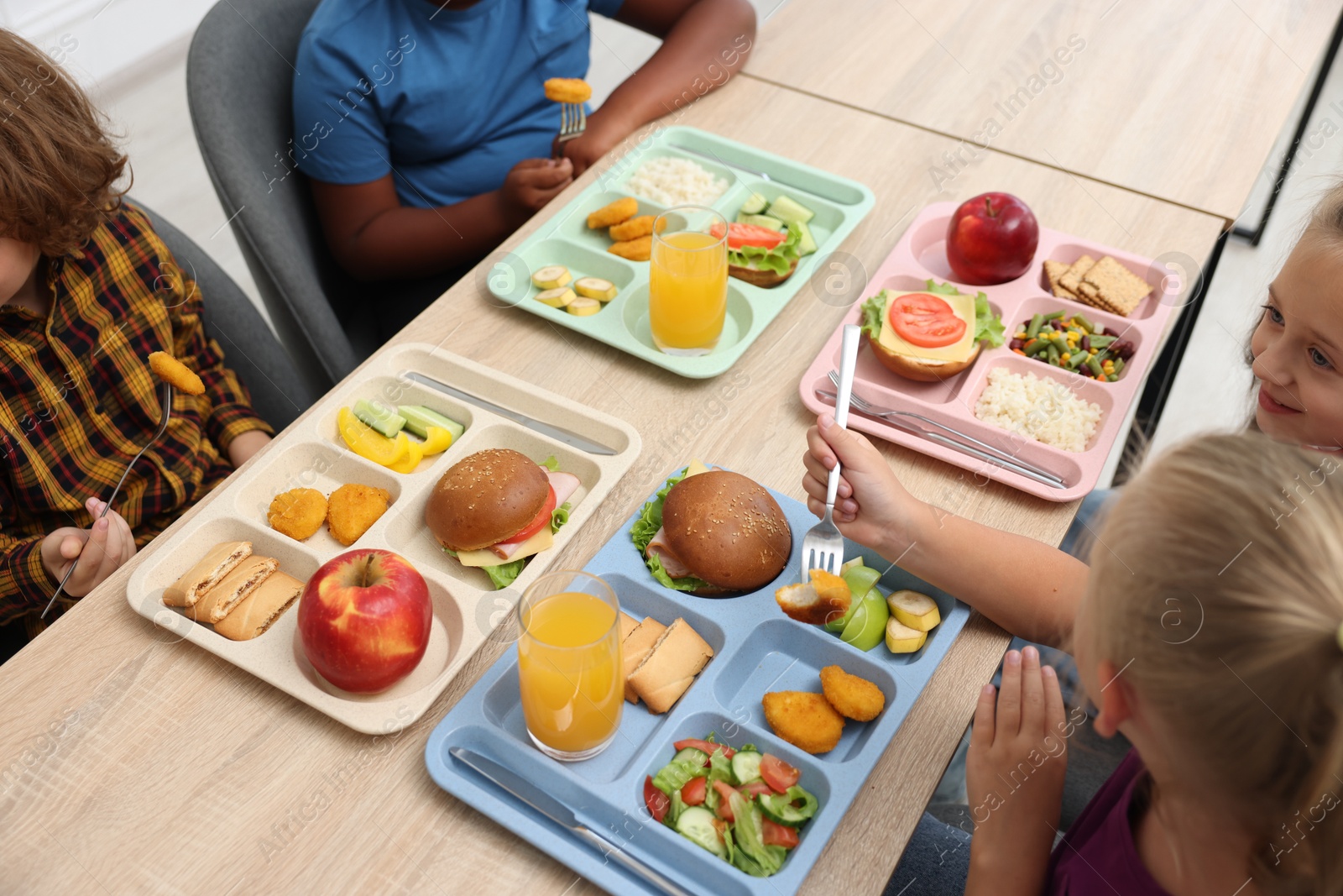 Little kids eating lunch at wooden table in school canteen, closeup Photo of Little kids eating lunch at wooden table in school canteen, closeup