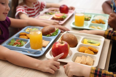 Photo of Little kids eating lunch at wooden table in school canteen, closeup