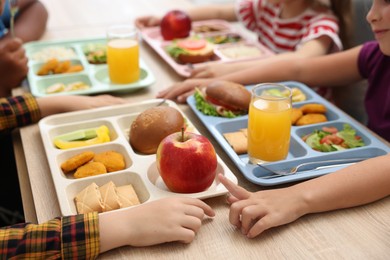 Photo of Little kids eating lunch at wooden table in school canteen, closeup