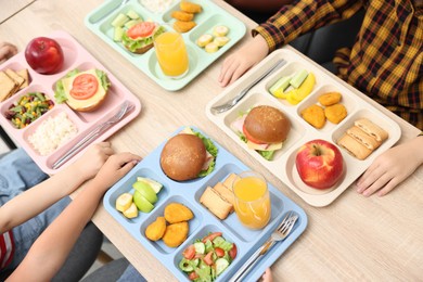 Photo of Little kids eating lunch at wooden table in school canteen, closeup