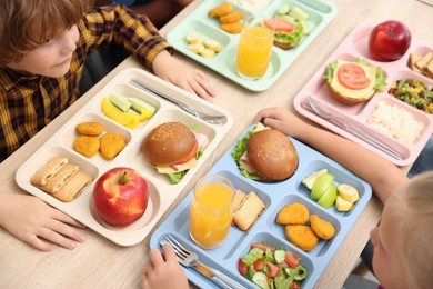 Photo of Little kids eating lunch at wooden table in school cafeteria, above view