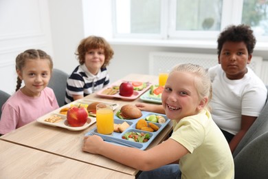 Photo of Little kids eating lunch at wooden table in school canteen