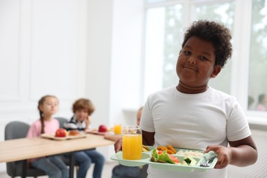 Photo of Little boy with tray of tasty food in school canteen