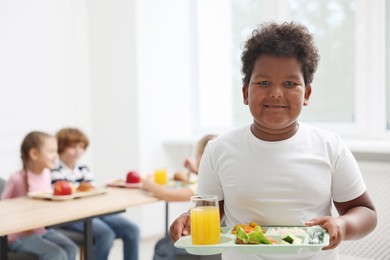 Photo of Little boy with tray of tasty food in school canteen