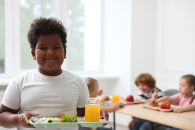 Photo of Little boy with tray of tasty food in school canteen