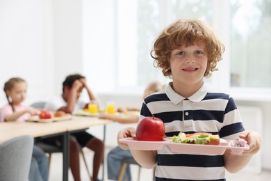 Photo of Little boy with tray of tasty food in school canteen
