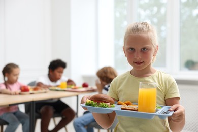 Photo of Little girl with tray of tasty food in school canteen