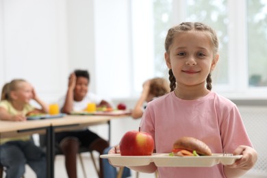 Photo of Little girl with tray of tasty food in school canteen