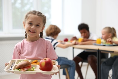 Photo of Little girl with tray of tasty food in school canteen