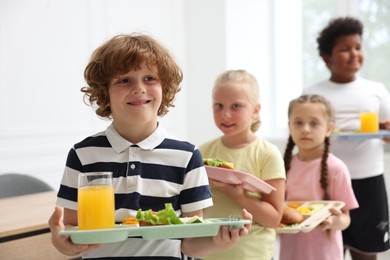 Photo of Little kids with trays of tasty food in school canteen, selective focus