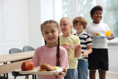 Photo of Little kids with trays of tasty food in school canteen, selective focus