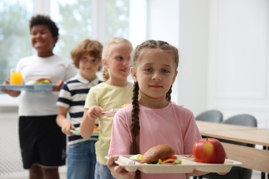 Photo of Little kids with trays of tasty food in school canteen, selective focus