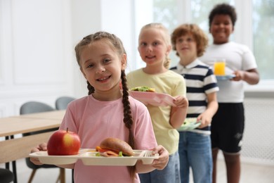 Photo of Little kids with trays of tasty food in school canteen, selective focus
